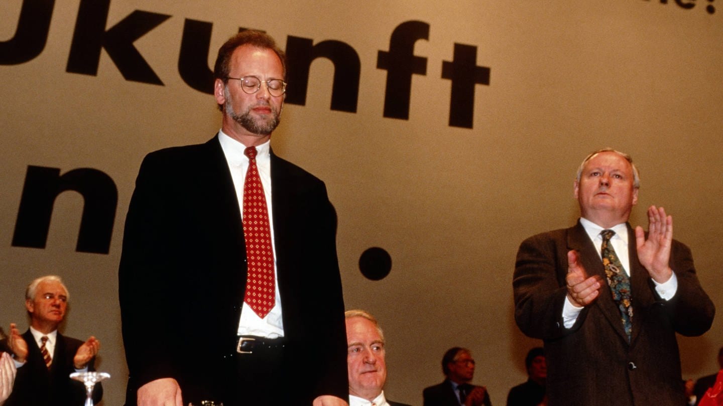 Der geschlagene und abgewählte Rudolf Schwarping (links) nimmt den Applaus von Oskar Lafontaine entgegen auf dem Parteitag der SPD am 16.11.1995 in Mannheim. In der Mitte Johannes Rau.