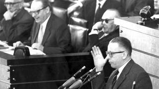 Der SPD-Abgeordnete Dr. Gustav Heinemann als erster Redner des Tages während der Fortsetzung der großen außenpolitischen Debatte im Deutschen Bundestag in Bonn am 25.3.1958. Im Hintergrund Bundeskanzler Konrad Adenauer (mit Sonnenbrille), Außenminister Heinrich von Brentano (M) und Justizminister Fritz Schäffer. Heinemann lehnte in seiner Rede die Fragestellung des Bundeskanzlers, NATO oder nicht, als Kernpunkt der Politik ab. Vor einer Sitzungspause am vorangegangenen Wochenende war im Bundestag bereits 28 Stunden lang leidenschaftlich über die politische Situation der Bundesrepublik, die Wiedervereinigung und die atomare Ausrüstung der Bundeswehr debattiert worden.