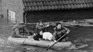 Eine Frau wird während der Sturmflut am 17. Februar 1962 mit einem Schlauchboot in Sicherheit gebracht. Das Wasser reicht fast bis zum Dach des Backsteinhauses im Hintergrund