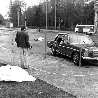 Der Tatort mit den zugedeckten Leichen von Siegfried Buback (vorne links) und seines Fahrers Wolfgang Göbel sowie der Dienstwagen des Generalbundesanwaltes, in dem die beiden erschossen wurde. Der höchste Ankläger der Bundesrepublik ist am 7. April 1977 in Karlsruhe durch Schüsse aus einer Maschinenpistole, die von einem Motorrad aus auf seinen Dienstwagen abgegeben worden waren, getötet worden. Mit ihm starb sein Fahrer Wolfgang Göbel, der lebensgefährlich verletzte Justizhauptwachtmeister Georg Wurster erlag am 13. April seinen Verletzungen.