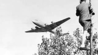 Berliner Luftbrücke: Ein Junge verfolgt von einem Baum aus den Landeanflug eines US-amerikanischen Transportflugzeugs auf den Berliner Flughafen Tempelhof. 