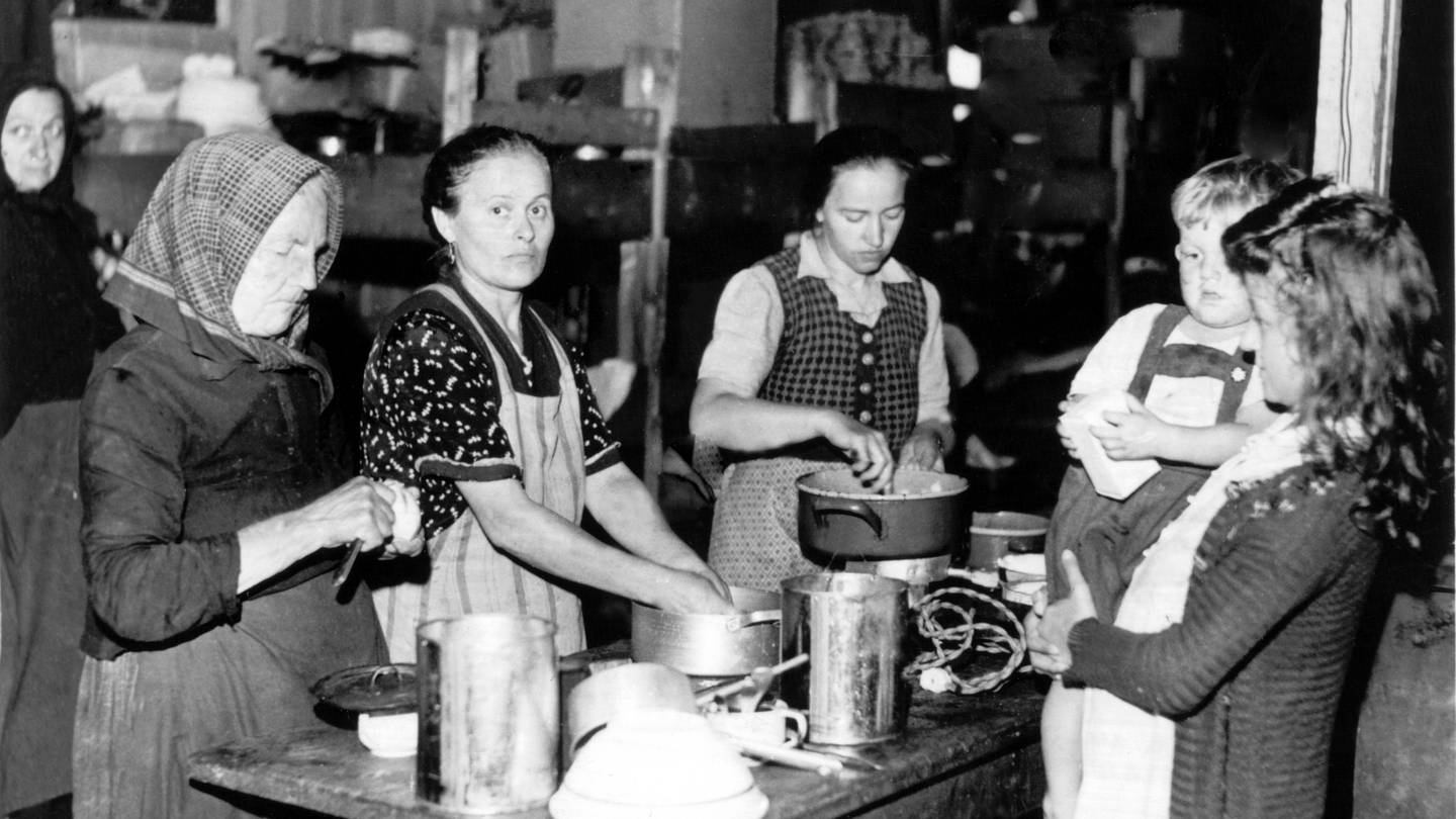 Frauen bereiten 1948 an einem Tisch im bayerischen Flüchtlingslager Allach Mahlzeiten zu (undatierte Aufnahme von 1948)