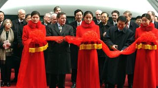 Bundeskanzler Gerhard Schröder (links) und der chinesische Ministerpräsident Zhu Rongji (rechts) schneiden am 31.12.2002 vor Beginn der Jungfernfahrt des Transrapids auf dem Bahnhof Longyang Lu in Schanghai ein rotes Band durch.