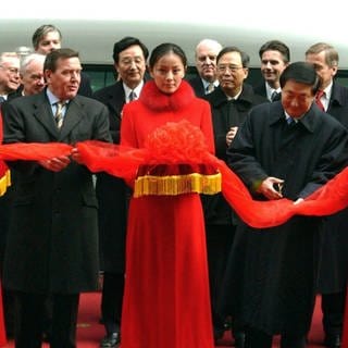 Bundeskanzler Gerhard Schröder (links) und der chinesische Ministerpräsident Zhu Rongji (rechts) schneiden am 31.12.2002 vor Beginn der Jungfernfahrt des Transrapids auf dem Bahnhof Longyang Lu in Schanghai ein rotes Band durch.