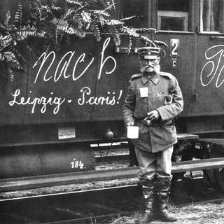 Soldat im Ersten Weltkrieg vor einem Zug mit der Aufschrift "Nach Paris – Leipzig  Paris!"