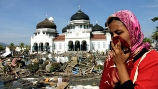 Eine Frau bedeckt ihre Nase mit einem Tuch; im Hintergrund eine Moschee. In den Straßen ist der Müll zu sehen, der sich nach dem Erdbeben und Tsunami in Banda Aceh auf der indonesischen Insel Sumatra im Dezember 2004 angesammelt hat.