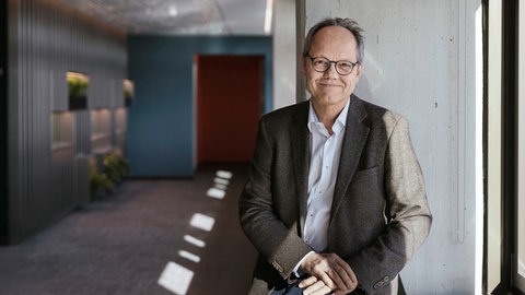 Der Intendant des SWR, Kai Gniffke, sitzt vor einer grauen Säule neben dem Fenster.