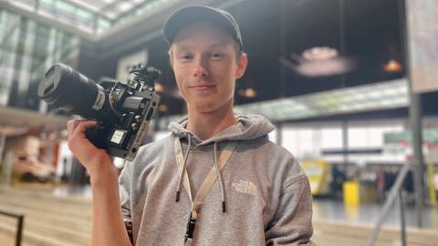 SWR Mediengestalter Azubi Leifur Seibt steht mit einer Kamera in der Hand auf der Stuttgarter Messe