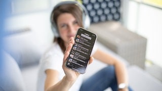 Eine Frau hält ein Smartphone mit der SWR2 App in der Hand