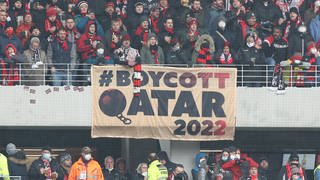 Menschen auf einer Fußballtribüne, am Geländer ein Transparent, auf dem "Boykott Qatar 2022" steht.