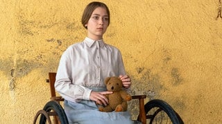 Martha Haberland als Margarete Steiff, im Rollstuhl sitzend, mit Teddybär in der Hand.