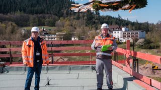 Zwei Herren in Helmen und in orangenen Sicherheitsjacken auf einer Baustelle