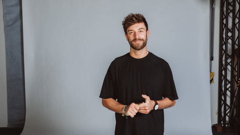 Journalist, Host und Moderator Frederic Fleig steht vor einer weißen Fotoleinwand.