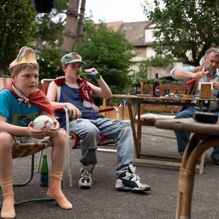 Christian (Camille Loup Moltzen), sein Bruder Benny (Len Blankenberg) und Opa Willy (André Eisermann) schauen Fernsehen