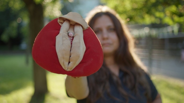 Eine Frau hält eine Schamlippe aus Plastik in der Hand