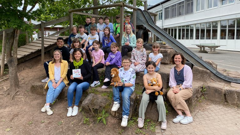 Klasse 3 a der Grundschule Winnweiler auf Hügel auf dem Schulhof, sitzend, zusammen mit Lehrerinnen und einer SWR-Redfakteurin