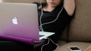 Laptop auf dem Schoß einer jungen Frau, daneben ein Handy: Wenn es um den Schutz ihrer Online-Konten geht, sind die meisten Menschen in Deutschland sorglos