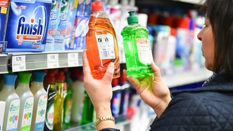 Eine Frau prüft im Supermarkt die Etiketten von zwei Spülmittelflaschen