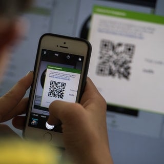 Eine Person hält ein Smartphone vor einen QR-Code und scannt diesen mit der Handykamera.