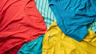 Shirts mit verschiedenen Farben liegen aufeinander gestapelt. Funktionsshirts aus Merino sollen eine optimale Wärmeregulation haben und geruchsneutral sein. Aber wie sieht es bei der Haltung der Tiere und Schadstoffen aus?