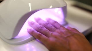 Eine Frau hält ihre Hand unter eine kleine UV-Lampe, um die lackierten Nägel zu trocknen.