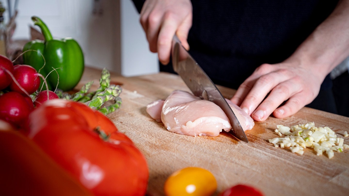 Eine Person schneidet ein Stück Fleisch auf einem Holz-Schneidebrett. Ein Labortest zeigt: Viele Schneidebretter in der Küche aus Holz oder Plastik sind mit Keimen belastet. Welches Brett sich wofür eignet und was man bei der Reinigung beachten sollte.