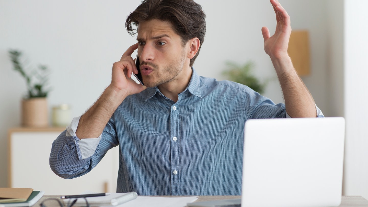 Junger Mann in blauem Hemd vor Laptop telefoniert und gestikuliert wütend am Handy. Was ist die neue Abhilfeklage? Wie können Sie gegen Vodafone, Facebook & Co. vorgehen?