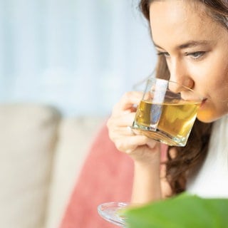 Junge Frau trinkt hellen Tee aus gläserner Tasse. Kräutertees von Meßmer, Teekanne, Westminster, Lord Nelson, Captains Tea und Mayfair im Test.