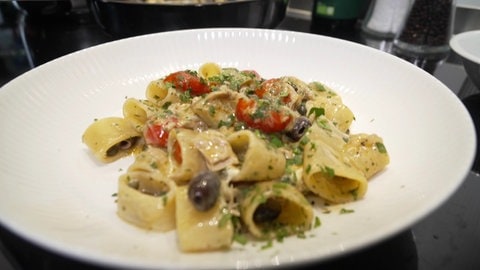 Nahaufnahme von Pasta Calamarata mit Thunfisch und Burrata. Serviert auf einem weißen Teller.