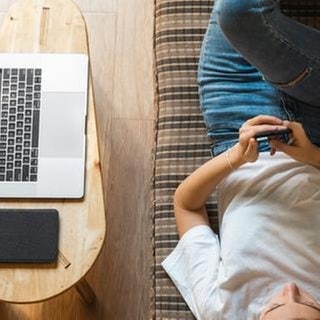 Frau mit Notebook und Smartphone auf dem Sofa