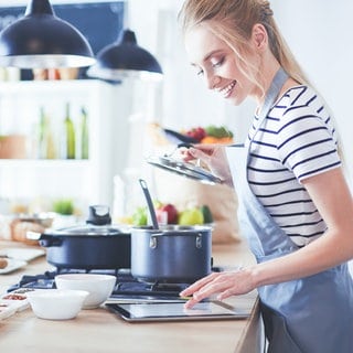 Eine Frau kocht und schaut sich ein Rezept auf dem Tablet an