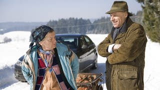 Lioba zieht ihr Wägelchen an Franz vorbei, der im Schnee vor seinem Auto steht 