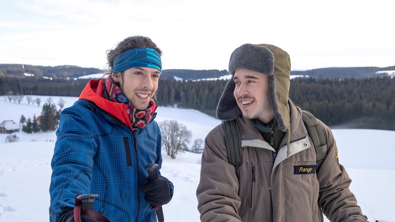 Albert und Sebastian stehen in verschneiter Landschaft. 