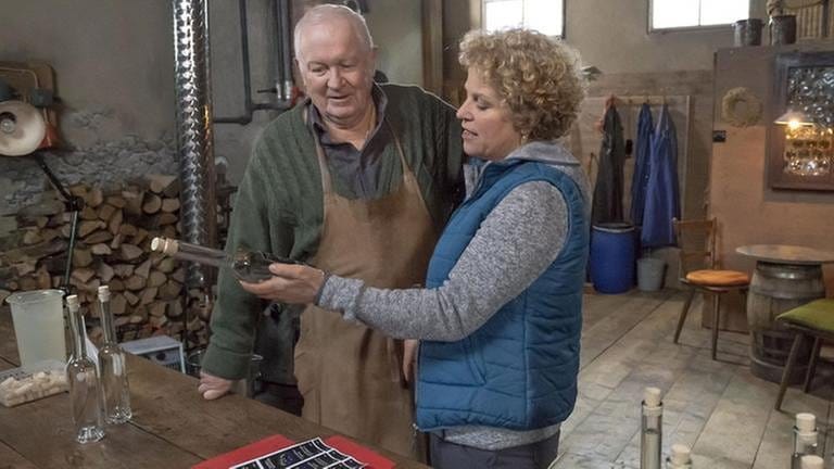 Zimmermann Senior und Bea betrachten eine Flasche von ihrem gemeinsam gebrannten Schnaps