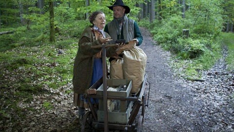 Lioba und Toni mit einem Leiterwagen im Wald, Lioba zeigt Toni Kohlestücke