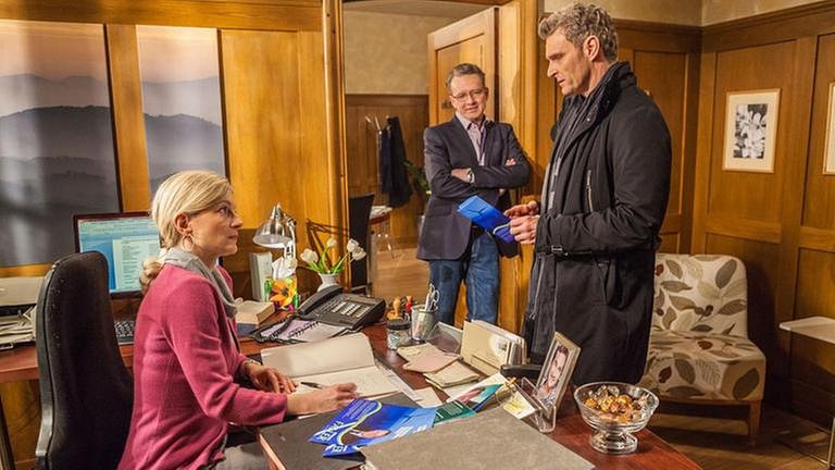 Frau Heilert, Bernhard und Uli Zimmermann in Frau Heilerts Büro, Zimmermann hält einen Flyer in der Hand