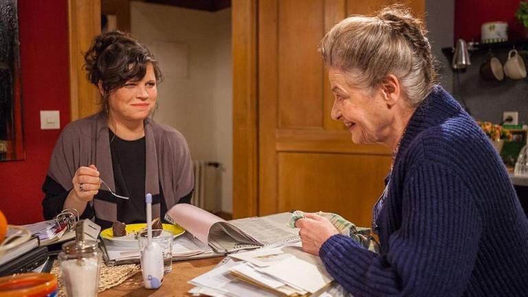 Johanna und Eva sitzen an Evas Küchentisch und essen Kuchen