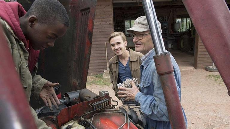 Tayo schaubt an Karls Traktor herum, Karl und Sebastian stehen beeindruckt daneben