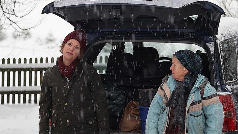 Bea und Lioba hinter dem geöffneten Kofferraum von Beas Auto, es schneit