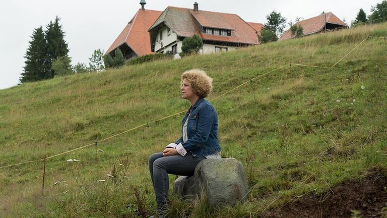 Bea sitzt unterhalb des Fallerhofes auf einem großen Stein