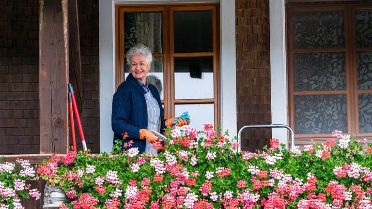 Johanna steht auf dem Balkon, die Geranien blühen üppig