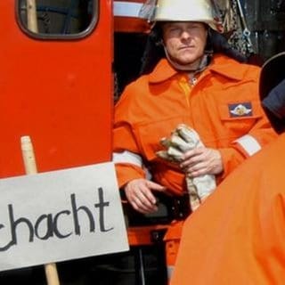 Bea und Tom sitzen in Feuerwehruniform vor einem Feuerwehrauto