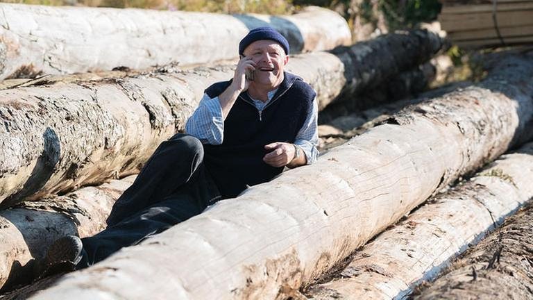 Tony liegt auf Holzstämmen und telefoniert