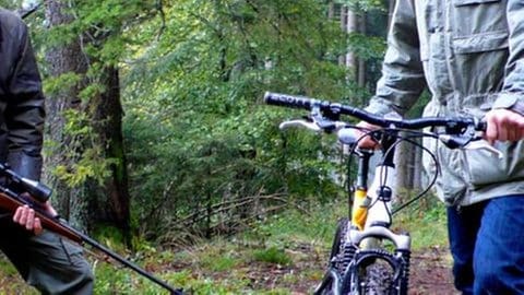 Bernhard mit Gewehr und Karl mit Fahrrad im Wald