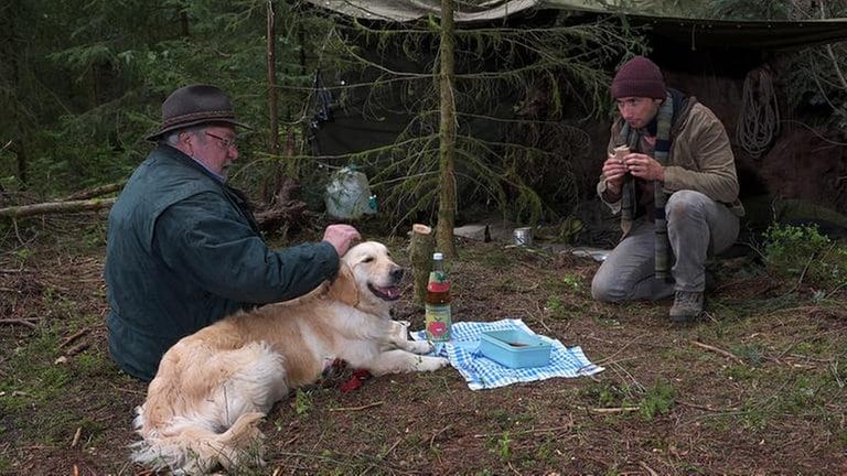 Hermann sitzt mit Willy bei einem Fremden im Wald