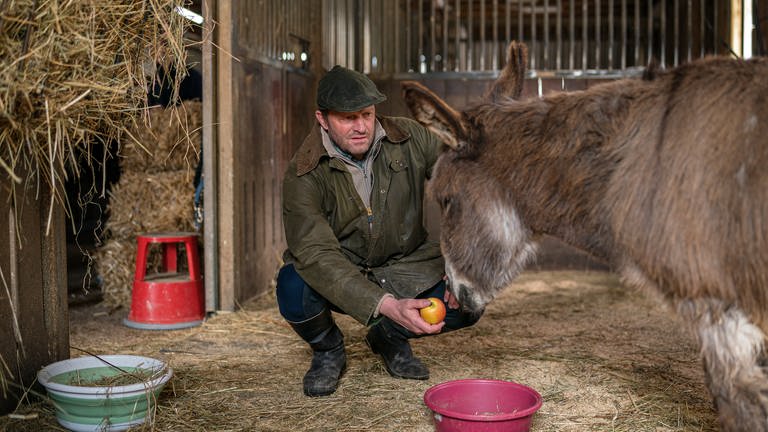 Bernd kniet mit Futter vor der blinden Eseldame Bonnie