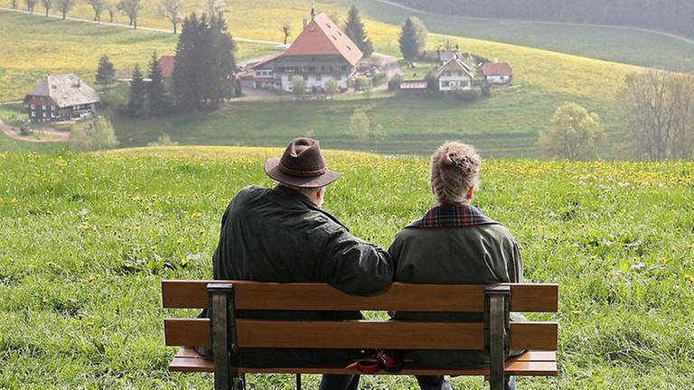 Hermann und Johanna sitzen auf einer Bank und blicken auf den Fallerhof