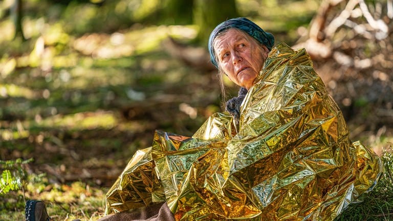 Lioba sitzt mit goldener Wärmefolie um die Schultern im Wald