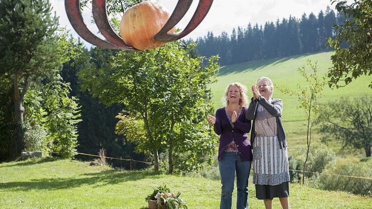 Johanna und Bea bestaunen einen in einer Greifzange eines Schleppers hängenden Kürbis