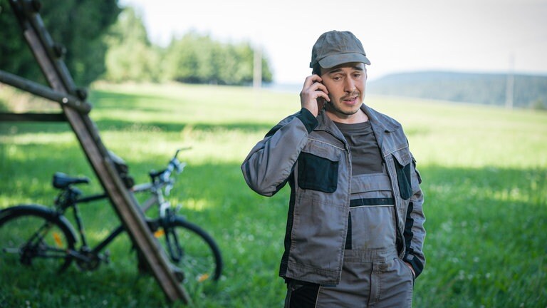 Sebastian steht telefonierend bei einem Hochsitz, an dem sein Fahrrad lehnt